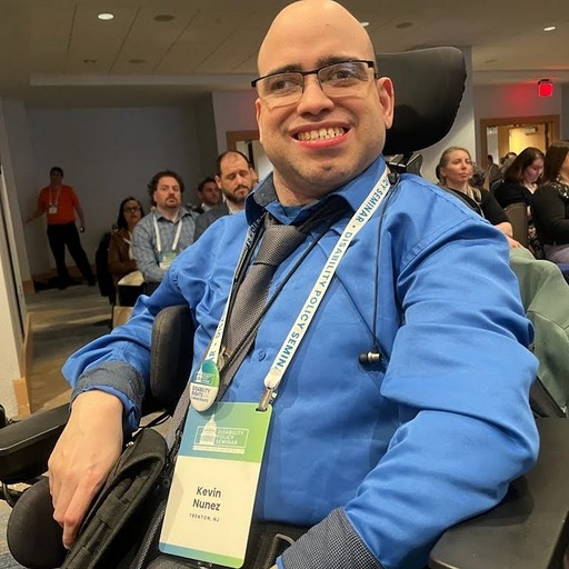 Smiling caucasian man wearing glasses and a blue shirt sitting in a wheelchair