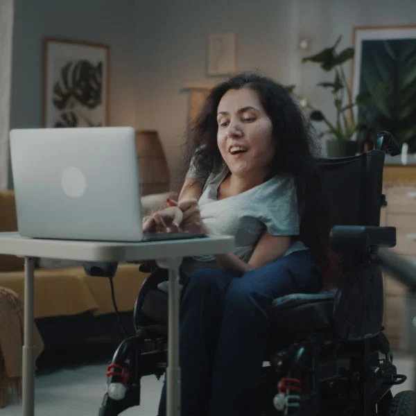 Woman with dark hair in wheelchair and typing on a laptop
