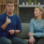 portrait-of-positive-attractive-married-couple-with-hearing-loss-sitting-on-sofa-commu-SBI-351619707
