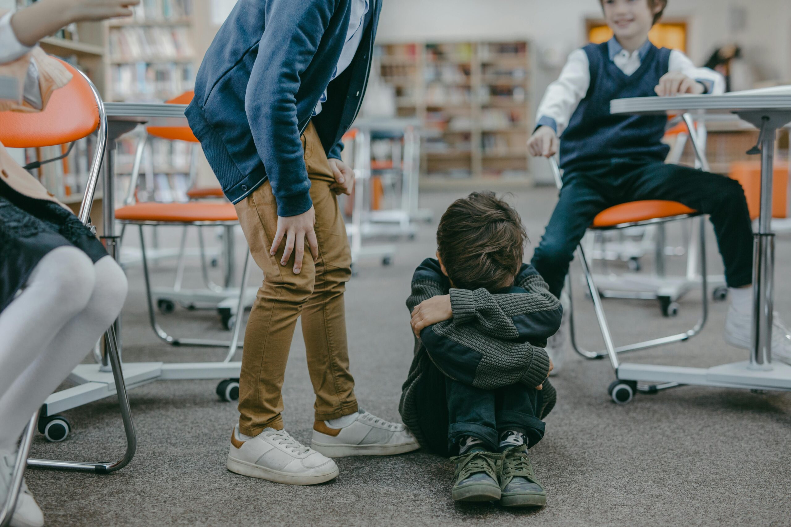 scared child sitting on the ground and hiding their face while adult stands nearby offering assistance